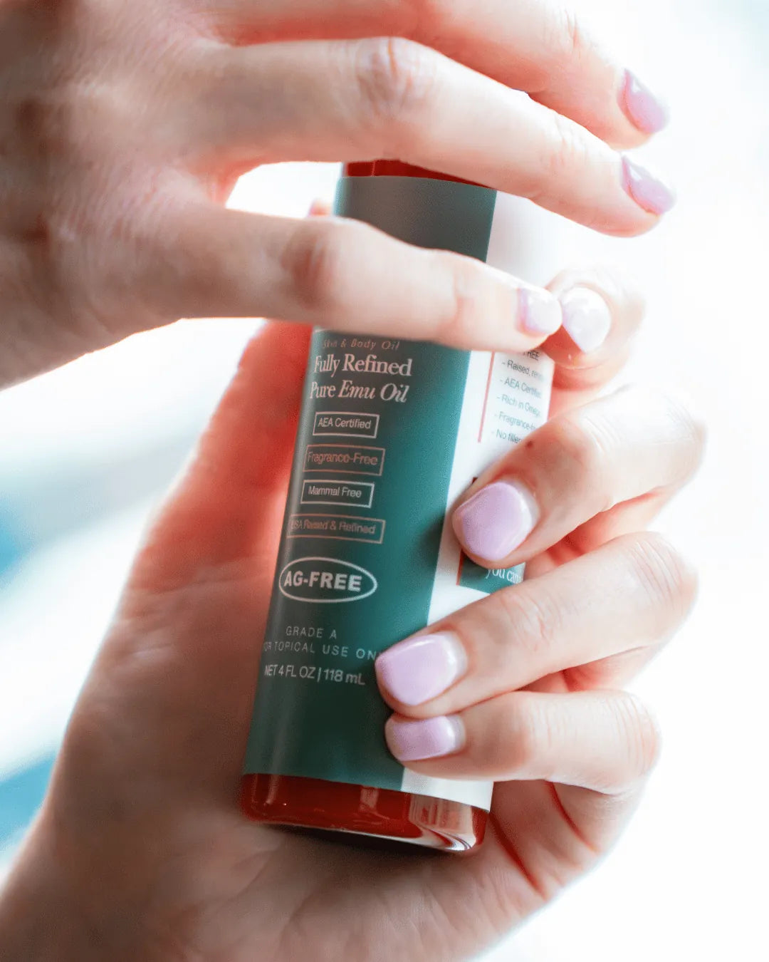 Hands with light purple nails holding a bottle of Amaroo Naturals pure emu oil