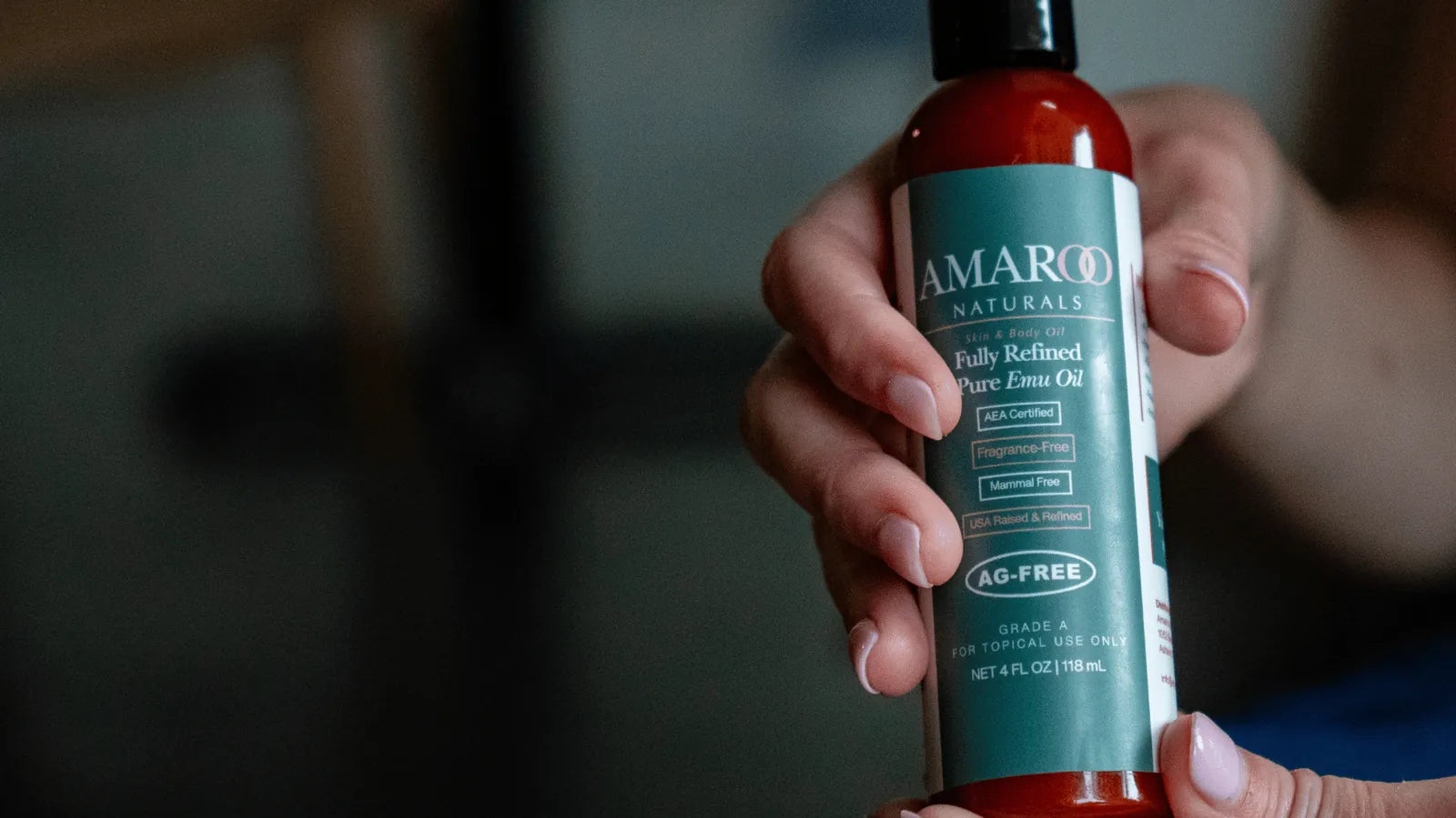 A person holding a bottle of AG-FREE® Amaroo Naturals emu oil and reading the label